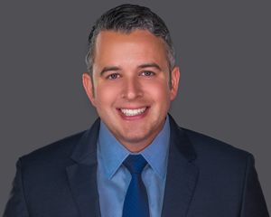 Headshot of a male healthcare lawyer in a navy blue suit and tie smiling.