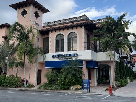 The front entrance of Di Pietro Partners. It's a pink and white building surrounded by palm trees with a sign that says Di Pietro Partners attorneys at law