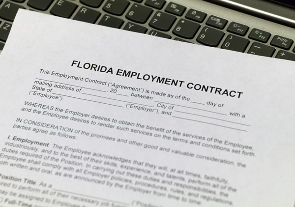 An employment contract sits on a laptop keyboard, waiting to be completed