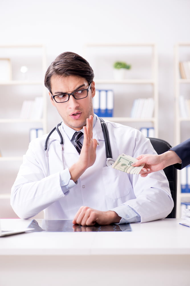 Doctor with black rimmed glasses in a white lab coat refusing to accept payment from an off screen person