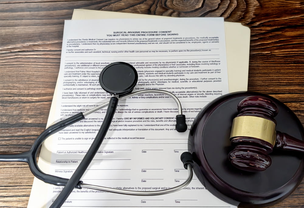 A surgical informed consent form on a desk with a stethoscope and a judge’s gavel placed on top symbolizing medical malpractice